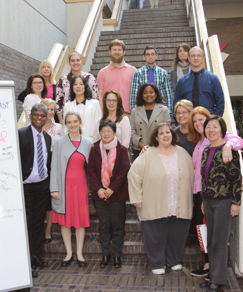 Group of library staff poses on stairs for breast cancer awareness day